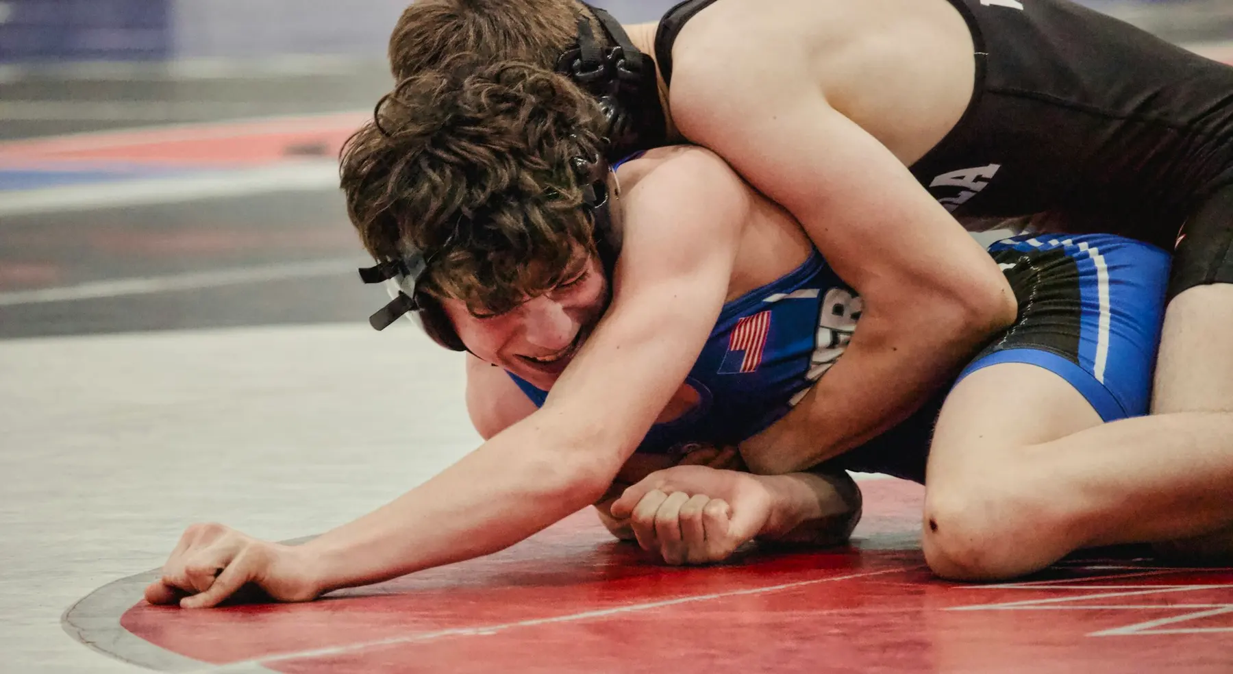 A wrestler reaches for the mat while being held in a tight tie-up.